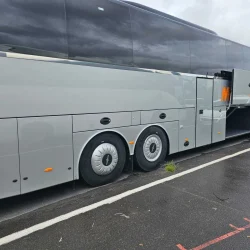 Side view of a VanHool bus with open luggage compartments for easy access to storage areas.